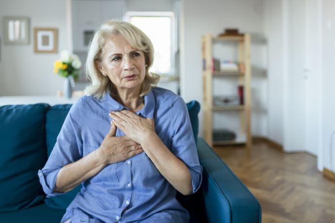 Une dame âgée est assise dans le canapé et a des douleurs dans la poitrine