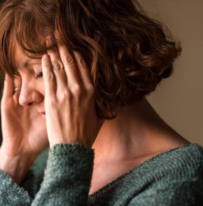 Une femme aux cheveux courts châtain souffre de maux de tête et se frictionne les tempes